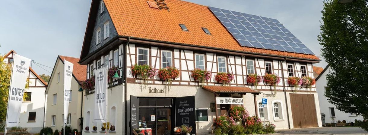 Blick auf den Dorfladen von Außen, ein Fachwerkhaus mit Blumenkübeln an den Fenstern und Solarmodulen auf dem Dach.