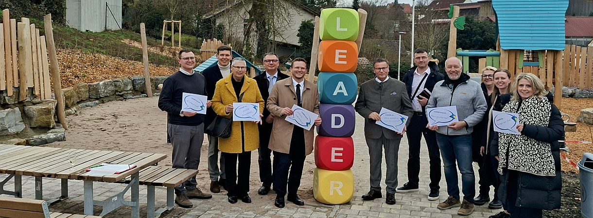 Menschen auf einem Spielplatz mit senkrecht aufgebauten Würfeln die das Wort LEADER ergeben