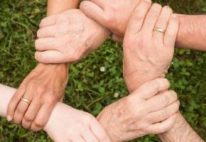 Blick von oben auf mehrere Hände, die sich an den Hanfgelenken fassen und einen Kreis bilden
