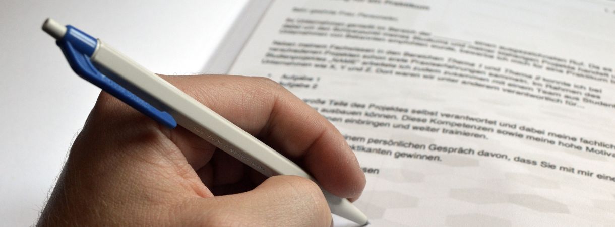 Hand mit Stift in der Hand, die ein Formular unterschreibt