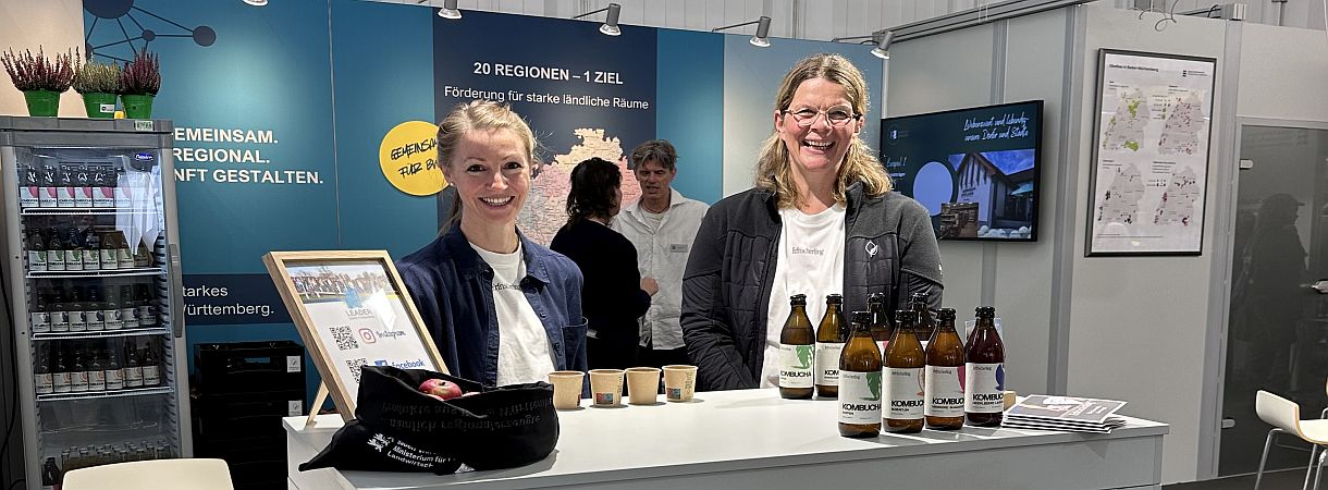 Messestand, zwei Personen hinter einem Tresen, mehrere Flaschen auf dem Tresen