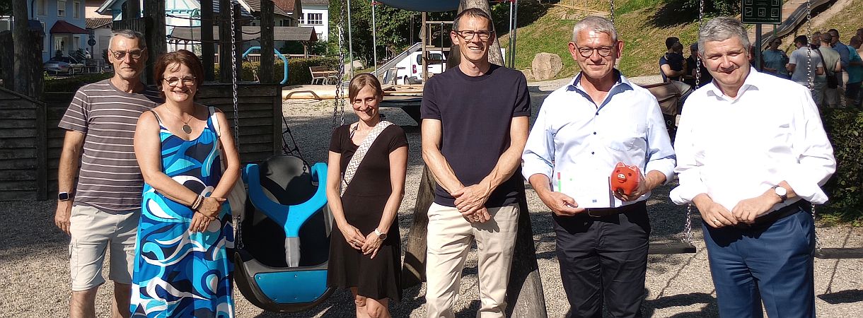 Im Vordergrund sechs Personen nebeneinander stehend, im Hintergrund ist der Spielplatz zu sehen